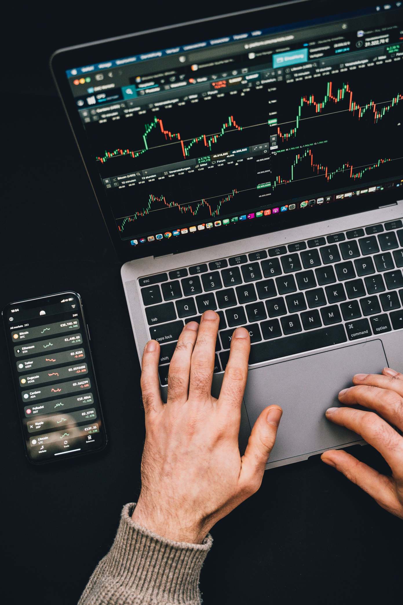 Hände tippen auf Laptop mit Finanz-Charts und Smartphone-Anzeige